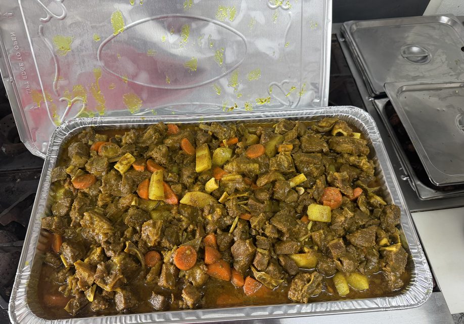 A foil tray of curry goat with carrots and potatoes