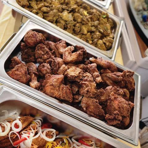 A catering line seen down its length: escovitch fish, fried chicken, curry, jerk and rice and peas in warmers