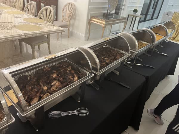 A catering line set out on black-draped tables at a venue, chafing dishes down the row